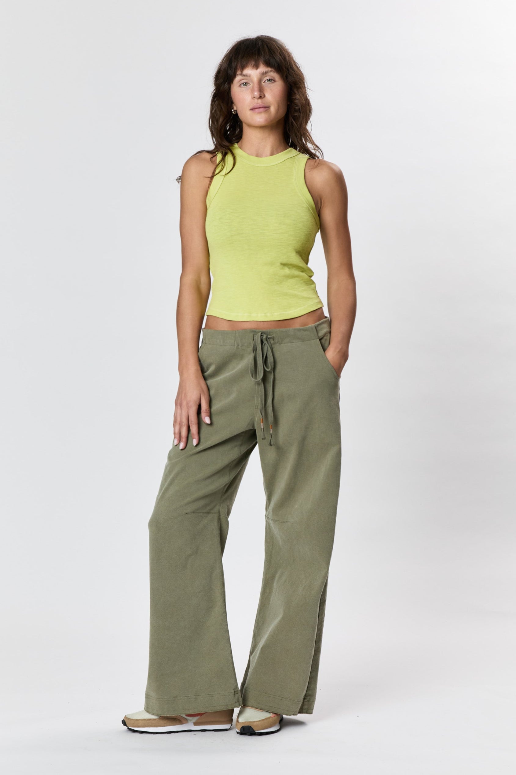 Woman wearing a green sleeveless top and olive green pants on a white background